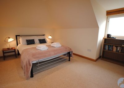 Large bed beneath coved ceiling. There is a bookcase beneath a window.
