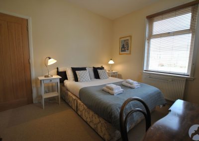 Double bed between white bedside tables and lamps. To the left is a door, and to the right a window.