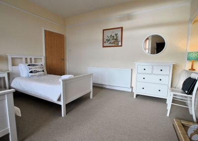 Two single beds separated by a bedside table. There is a round mirror on the wall above a chest of drawers and next to a long radiator.