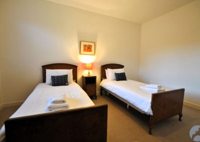 Two single beds with dark wood and white linen either side of a narrow bedside table with a lamp.