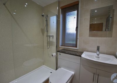 White bathroom suite. Shower and clear shower screen to the left of a narrow window.