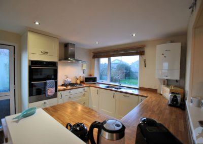 Square kitchen with light cabinet doors. There is a sink looking out to the garden through a wide window.