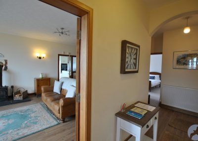 View from hallway into lounge on left and towards a bedroom at the end of the hallway. There is a table beneath a clock in the hall.