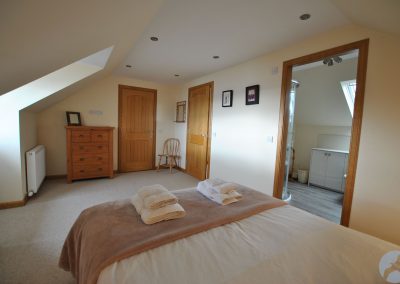 View from bed down the long bedroom beneath the eaves. There is an open door into the en-suite bathroom on the right and two doors at the far end of the room.