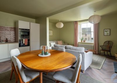 Round dining table with four seats. The lounge is behind it.