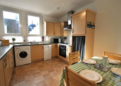 Wooden kitchen cabinets with white goods and a table set with crockery in the foreground.