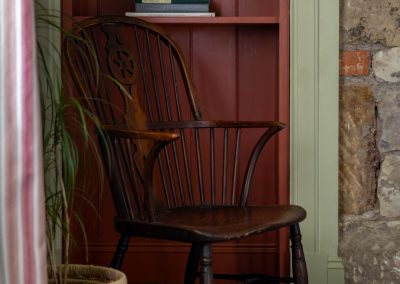 Deep red alcove bookcase with a chair in front, next to an exposed stone wall.