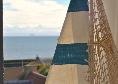 Close up of a model sailing boat. Beyond is a view across rooftops towards the sea.