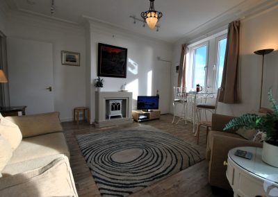 View across lounge towards a fireplace and large windows.