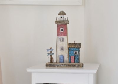 Narrow bookcase with model of lighthouse on top.