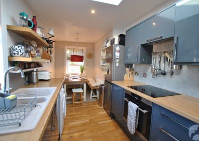 Bright dining kitchen with fitted units, wooden worktops and modern appliances, leading to a dining table set for four beneath a skylight.