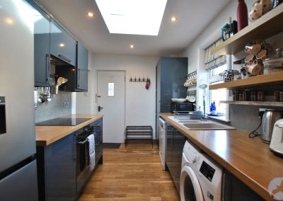 Galley-style kitchen with modern units, wooden worktops and integrated appliances, featuring a skylight and window providing bright natural light.
