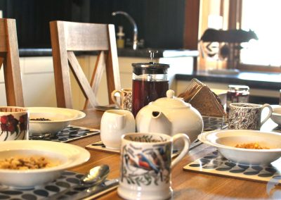 Breakfast table set with bowls, mugs, teapot, coffee press and slices of toast.